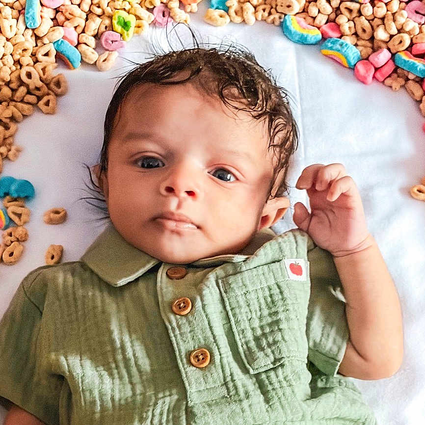 Davion is registered to the contest to win money with this photo: baby, breakfast_cereal, buttons, cereal_loops, child, closeup, colorful_marshmallows, cute, eyes, face, green_shirt, hair, hand, infant, lying_down, newborn, playful_setup, portrait, soft_texture, white_blanket