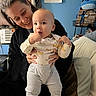 Amari is registered to the contest to win money with this photo: baby, infant, adult, parent, smiling, standing, portrait, indoor, bedroom, bed, pillow, plush_toy, stitch, cartoon, blue_wall, clothing, onesie, gray_pants, family, home