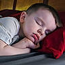 child, sleeping, pillow, bed, rest, peaceful, face, head, hand, young, indoors, cozy, red_pillow, gray_bedspread, relaxation, nap, portrait, tired, calm, soft_light
