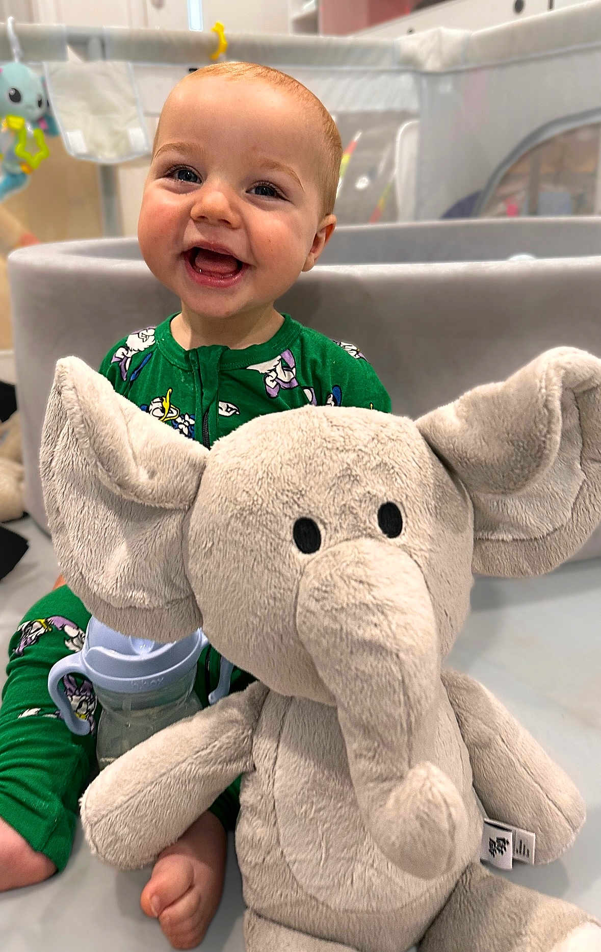 Arlo joined the competition — help win amazing prizes! baby, child, smiling, green_onesie, plush_elephant, toy, playpen, sippy_cup, indoor, floor, feet, happy, cute, infant, portrait, childhood, playtime, soft_toy, person, closeup
