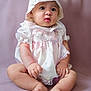 baby, infant, child, bonnet, dress, lacy_clothing, sitting, soft_background, curious_expression, barefoot, pink_tones, chubby_arms, chubby_legs, portrait, studio_photo, cute, innocence, closeup, indoor, person