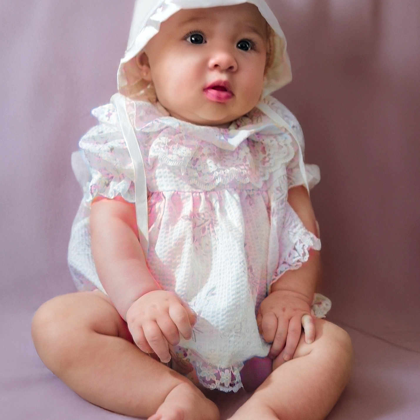 Shalynne is registered to the contest to win money with this photo: baby, barefoot, bonnet, child, chubby_arms, chubby_legs, closeup, curious_expression, cute, dress, indoor, infant, innocence, lacy_clothing, person, pink_tones, portrait, sitting, soft_background, studio_photo