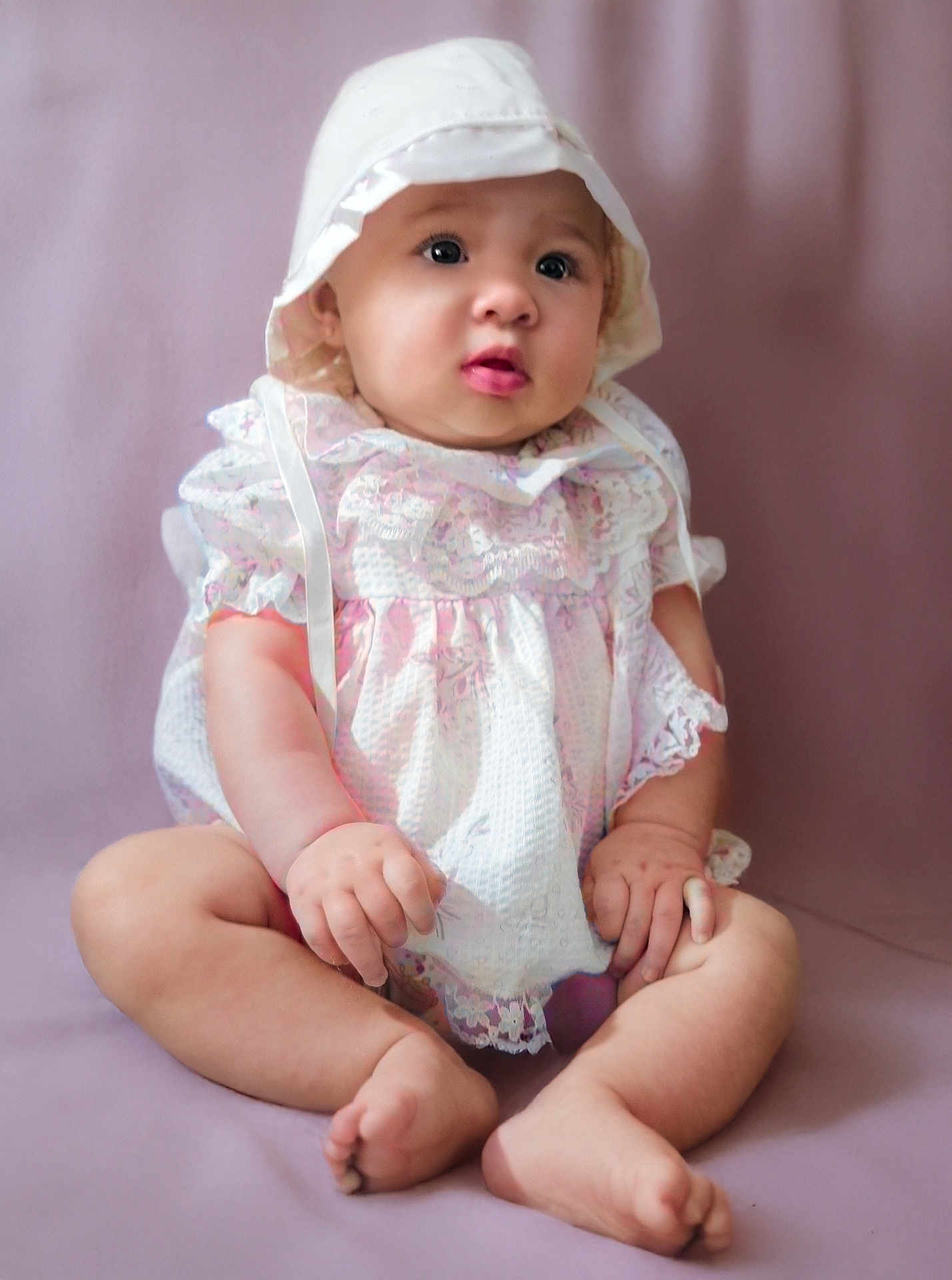 Shalynne is registered to the contest to win money with this photo: baby, infant, child, bonnet, dress, lacy_clothing, sitting, soft_background, curious_expression, barefoot, pink_tones, chubby_arms, chubby_legs, portrait, studio_photo, cute, innocence, closeup, indoor, person