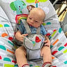 baby, infant, child, baby_seat, colorful, animal_print, rainbow, socks, blue_shirt, cute, indoors, seat_belt, toddler, playful, patterned_fabric, baby_toys, comfort, young_child, portrait, casual
