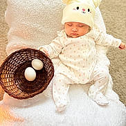 Adhara Luciana is registered to the contest to win money with this photo: baby, sleeping, hat, onesie, basket, eggs, blanket, carpet, soft_texture, cozy, cute, indoor, child, infant, resting, wearing, headwear, white, peaceful, adorable