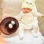 baby, sleeping, hat, onesie, basket, eggs, blanket, carpet, soft_texture, cozy, cute, indoor, child, infant, resting, wearing, headwear, white, peaceful, adorable