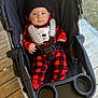 baby, child, stroller, red_clothing, black_clothing, hat, face, person, outdoor, wooden_deck, seatbelt, infant, cute, winter_clothing, plaid, portrait, sitting, headwear, bundle, serious_expression