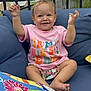 baby, child, smiling, sitting, outdoor, sofa, cushion, shirt, colorful, arms_up, happy, face, tree, sky, pillow, flower, bee, house, railing, shorts