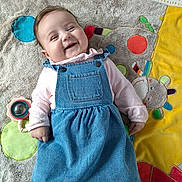 Lyanna a rejoint le concours — aidez-le/la à gagner de superbes lots ! baby, smiling, denim_dress, pink_shirt, play_mat, toy, happy, child, infant, lying_down, colorful, soft_texture, cute, indoor, portrait, person, clothing, face, baby_toy, playful