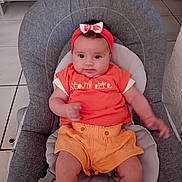 Ava participe au concours pour gagner de l'argent avec cette photo : baby, baby_chair, child, comfort, cute, face, grey_cushion, headband, home, indoor, infant, orange_clothing, person, pink_bow, portrait, seated, shorts, smiling, tiled_floor, young_child
