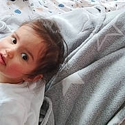 Laureline a rejoint le concours — aidez-le/la à gagner de superbes lots ! baby, bed, blanket, child, cozy, curious_expression, face, hair, indoor, looking_up, patterned_sheet, person, portrait, rosy_cheeks, sleepwear, soft_texture, star_pattern, toddler, white_clothing, young_child