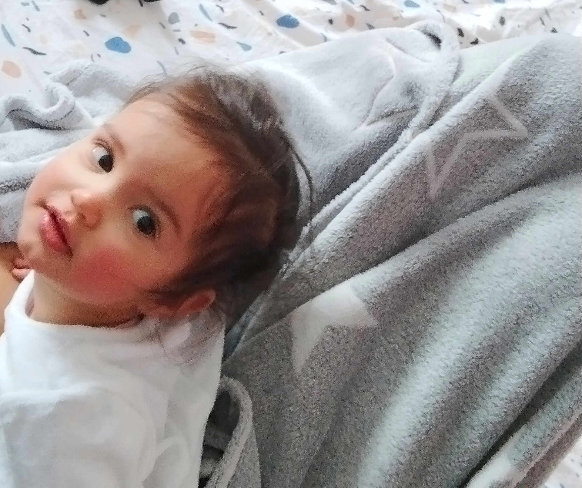 Laureline a rejoint le concours — aidez-le/la à gagner de superbes lots ! baby, bed, blanket, child, cozy, curious_expression, face, hair, indoor, looking_up, patterned_sheet, person, portrait, rosy_cheeks, sleepwear, soft_texture, star_pattern, toddler, white_clothing, young_child