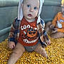 baby, child, hat, ears, plaid_jacket, orange_shirt, corn_kernels, sitting, indoor, curious, face, blue_eyes, clothing, autumn, playful, person, portrait, blurred_background, cute, toddler