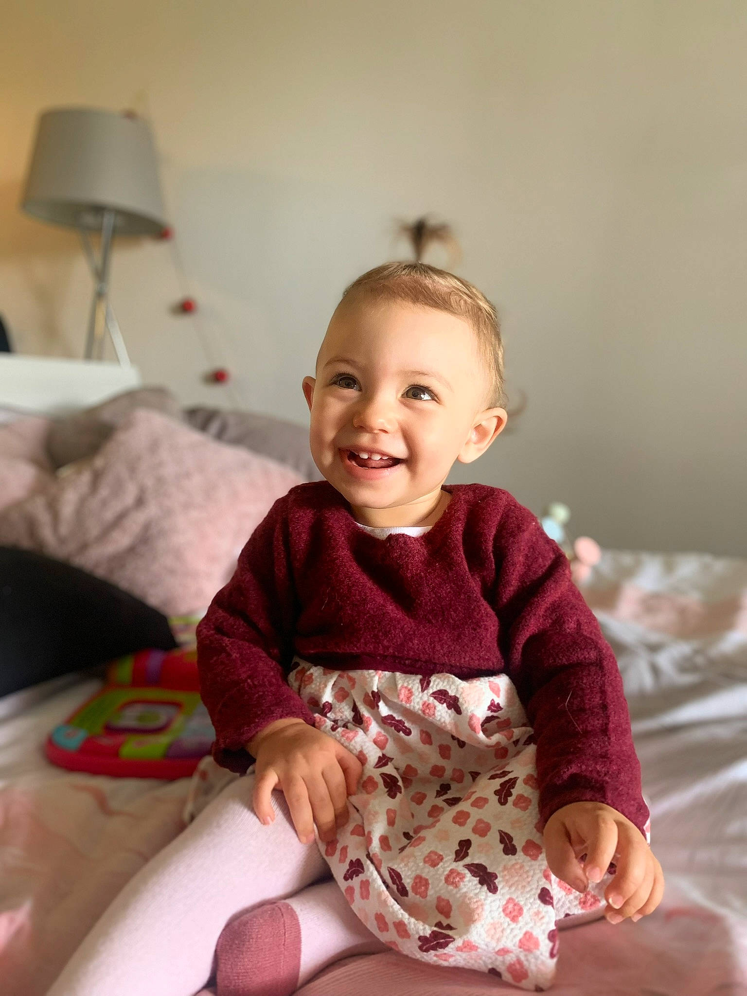 Aria participe au concours pour gagner de l'argent avec cette photo : baby, baby_toddler_clothing, child, comfort, dress, face, happy, head, human_leg, joy, knee, lamp, magenta, person, pink, room, sitting, skin, sleeve, smile