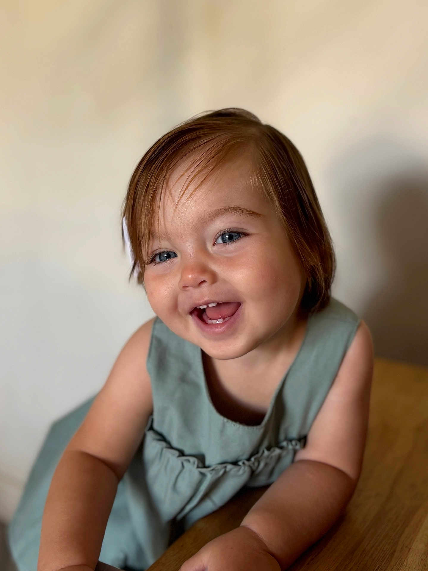 Emy participe au concours pour gagner de l'argent avec cette photo : toddler, child, smiling, portrait, blue_eyes, dress, short_hair, indoor, wooden_table, happy, cute, baby, skin, face, person, young_child, candid, expression, closeup, natural_light