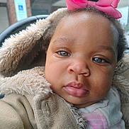 Samaya is registered to the contest to win money with this photo: baby, child, face, pink_bow, curly_hair, fuzzy_coat, warm_clothing, close_up, portrait, outdoor, expression, cute, infant, person, young_child, winter_wear, soft_texture, headwear, big_eyes, plump_lips
