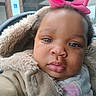 baby, child, face, pink_bow, curly_hair, fuzzy_coat, warm_clothing, close_up, portrait, outdoor, expression, cute, infant, person, young_child, winter_wear, soft_texture, headwear, big_eyes, plump_lips