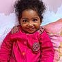 toddler, child, smiling, pink_jacket, curly_hair, indoor, cushion, floral_decor, crayon, cup, happy, portrait, seated, cute, holding, closeup, face, bright_colors, cozy, young