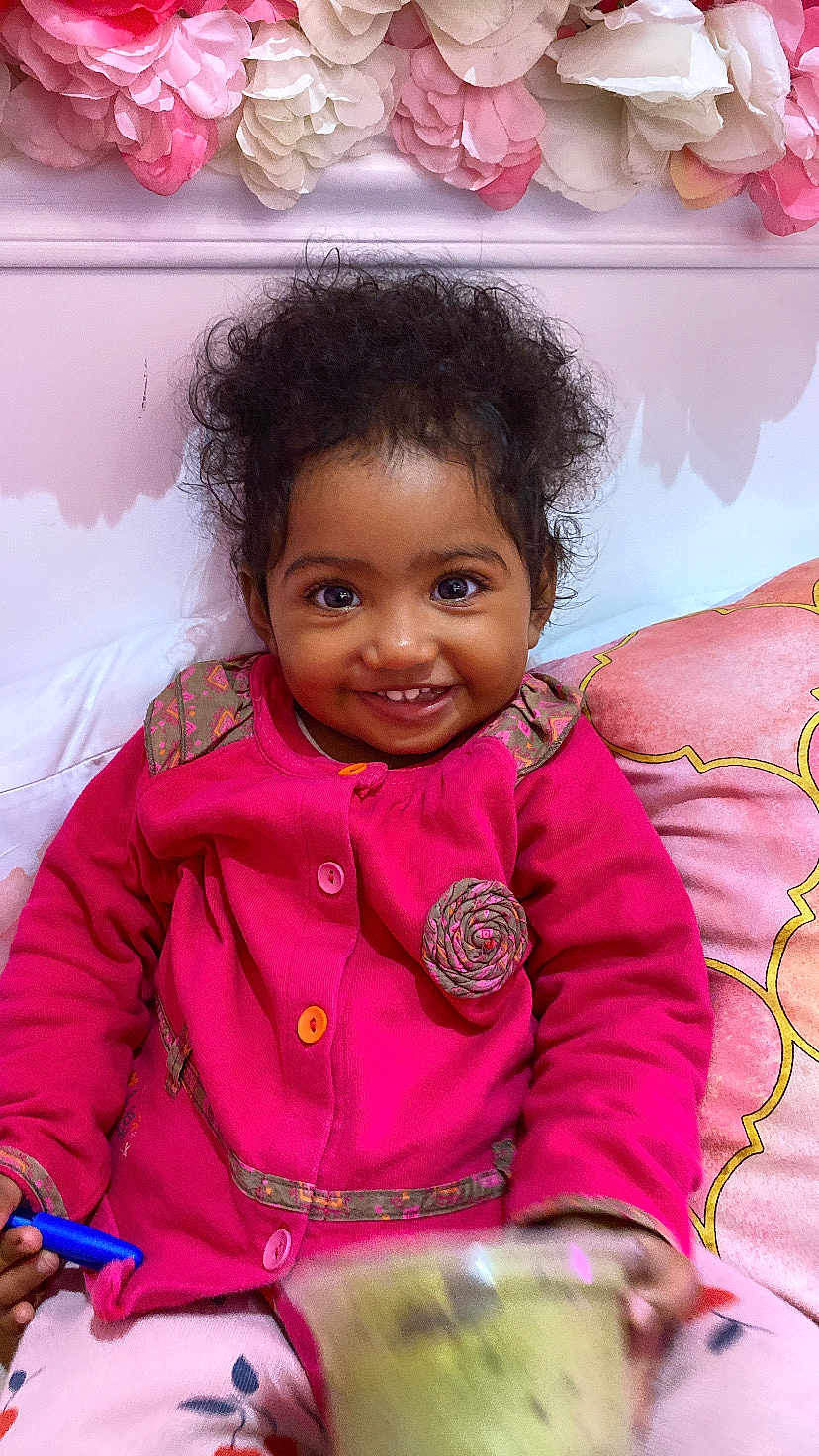 Mayanah participe au concours pour gagner de l'argent avec cette photo : toddler, child, smiling, pink_jacket, curly_hair, indoor, cushion, floral_decor, crayon, cup, happy, portrait, seated, cute, holding, closeup, face, bright_colors, cozy, young