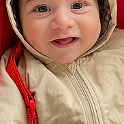 Ilyas is registered to the contest to win money with this photo: baby, child, smile, hood, jacket, blanket, face, eyes, cute, infant, warm_clothing, red_background, soft_texture, portrait, closeup, happy, cozy, young_child, person, indoor