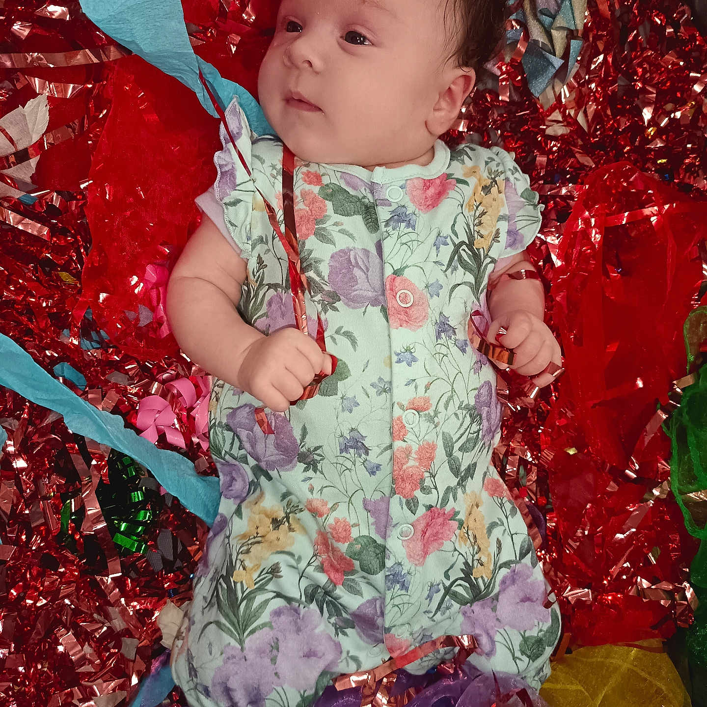 Setareh joined the competition — help win amazing prizes! baby, blue, celebration, colorful, cute, decorations, expression, face, festive, floral_onesie, hands, indoors, infant, lying_down, purple, red, ribbons, soft_lighting, streamers, yellow