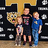 children, kids, group_portrait, smiling, happy, school, pre_k, siblings, standing, indoor, backdrop, leopard, paw_prints, gold_letter, casual_clothing, t_shirt, shorts, jeans, sneakers, photography