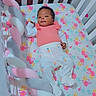 baby, crib, infant, floral, mattress, braided_bumper, pink, white, carrot_prints, clothing, sleepwear, cute, indoors, child, person, resting, smiling, head, hand, foot