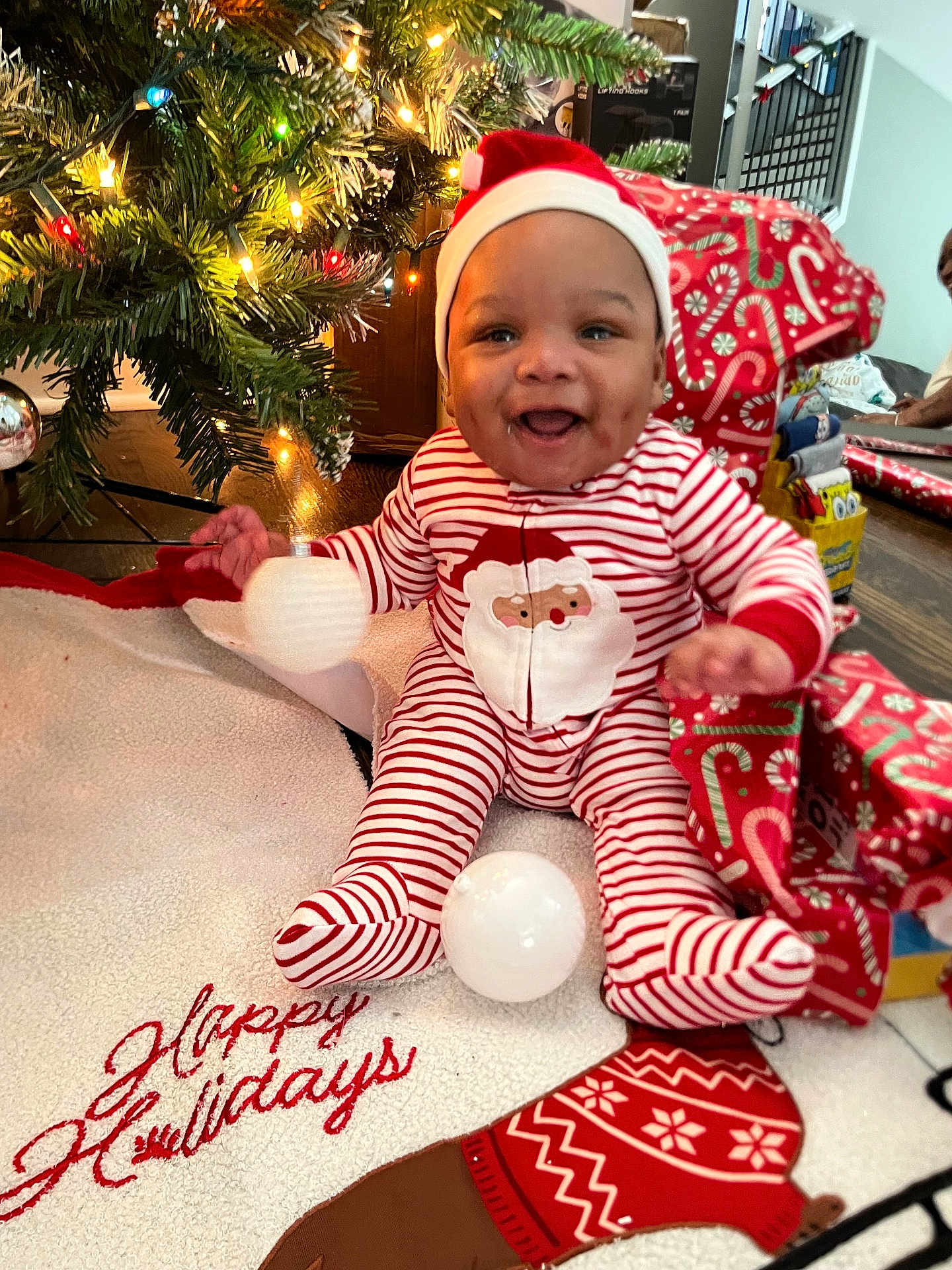 Chayce is registered to the contest to win money with this photo: baby, child, christmas_tree, christmas_lights, holiday, pajamas, santa_hat, smiling, gift_wrap, decorations, floor, indoors, festive, seasonal, happy, cute, person, celebration, red_and_white, christmas_stocking