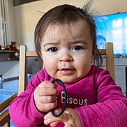 Séréna participe au concours pour gagner de l'argent avec cette photo : baby, chair, child, drool, eyes, face, hair_tie, hands, highchair, holding, indoor, living_room, messy_hair, mouth, nose, pink_shirt, portrait, television, toddler, wooden_table
