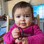 baby, chair, child, drool, eyes, face, hair_tie, hands, highchair, holding, indoor, living_room, messy_hair, mouth, nose, pink_shirt, portrait, television, toddler, wooden_table