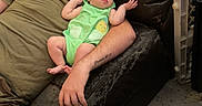 Diana is registered to the contest to win money with this photo: baby, infant, child, adult, parent, father, couch, sitting, lying_down, green_outfit, home, living_room, portrait, face, two_people, relaxed, game_controller, snacks, baby_gate, indoor