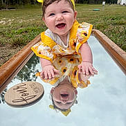Renley joined the competition — help win amazing prizes! baby, child, smiling, yellow_headband, sunflower_dress, mirror, reflection, outdoor, grass, forest, happy, portrait, person, nature, wooden_plaque, milestone, cute, infant, playful, bright_colors