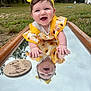 baby, child, smiling, yellow_headband, sunflower_dress, mirror, reflection, outdoor, grass, forest, happy, portrait, person, nature, wooden_plaque, milestone, cute, infant, playful, bright_colors