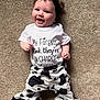 baby, child, smiling, headband, white_shirt, printed_text, cow_print_pants, carpet, lying_down, happy, cute, infant, person, indoors, playful, fashion, clothing, portrait, funny_text, closeup