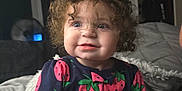 Lilith joined the competition — help win amazing prizes! toddler, child, curly_hair, blue_eyes, onesie, strawberry_pattern, bed, blanket, indoor, portrait, cute, smiling, baby, person, clothing, soft_lighting, cozy, face, sitting, curious