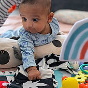 Noah is registered to the contest to win money with this photo: baby, child, toy, rubber_duck, play_mat, onesie, animal_prints, curious, infant, soft_toys, colorful, indoor, cute, hand, face, expression, pillow, striped, black_and_white, playtime