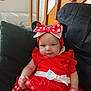 baby, child, red_dress, minnie_mouse, headband, bow, polka_dots, couch, indoor, stairs, wood, seated, cute, infant, clothing, person, face, expression, home, furniture