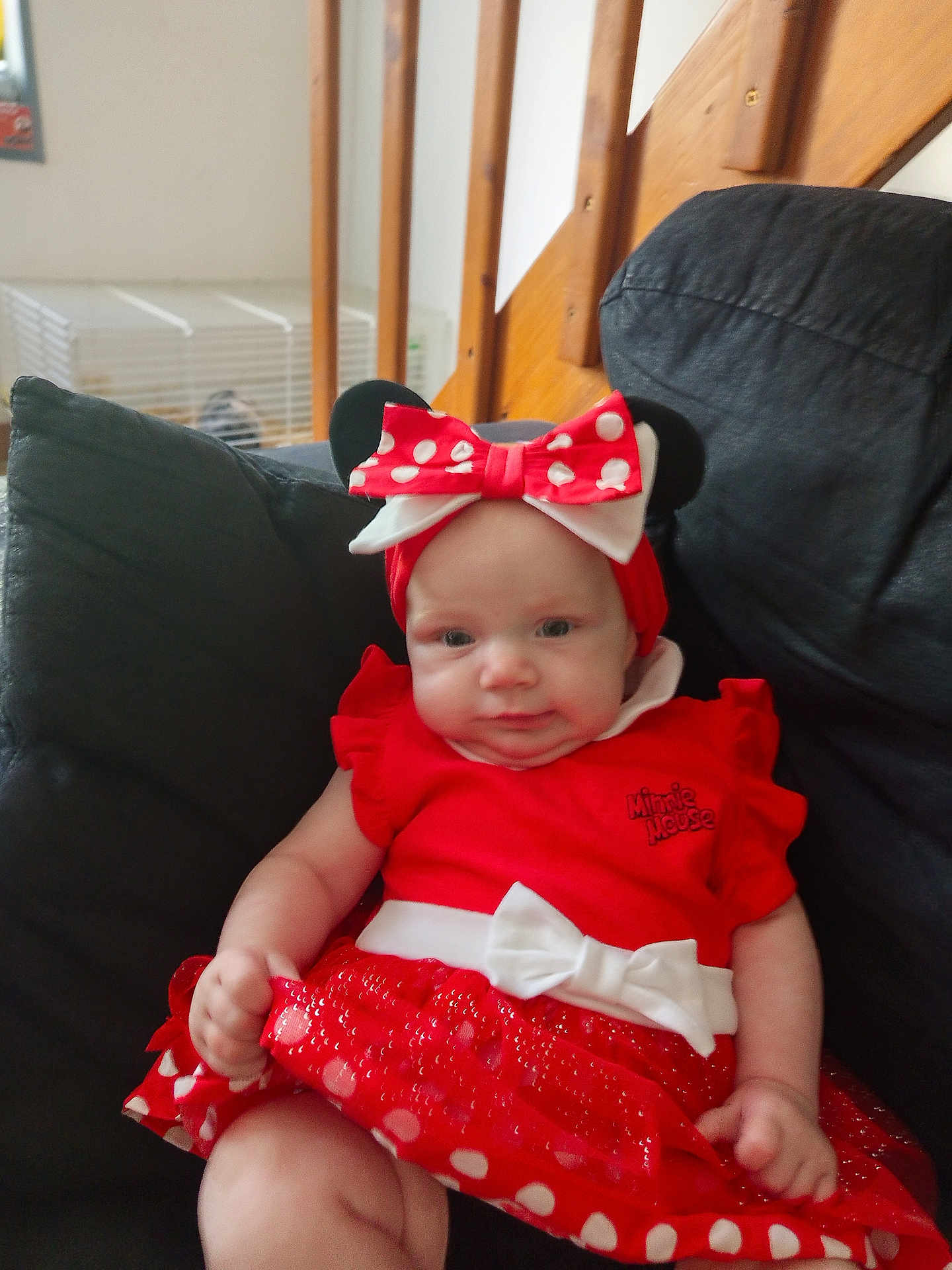 Mia participe au concours pour gagner de l'argent avec cette photo : baby, child, red_dress, minnie_mouse, headband, bow, polka_dots, couch, indoor, stairs, wood, seated, cute, infant, clothing, person, face, expression, home, furniture