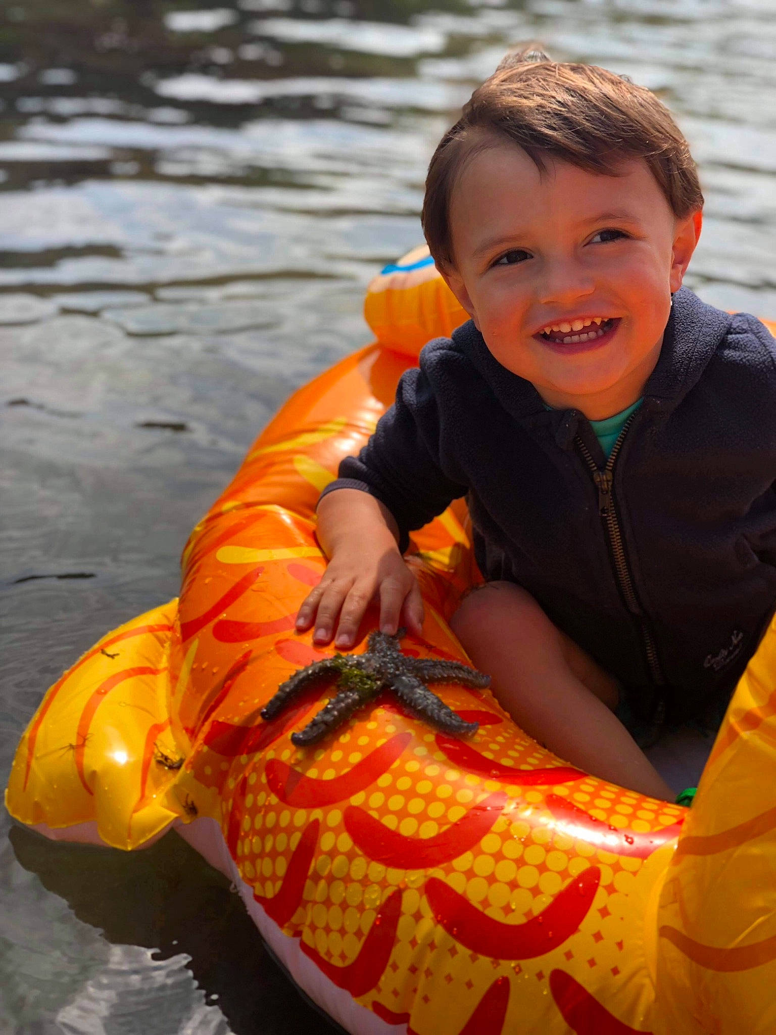 Etienne a rejoint le concours — aidez-le/la à gagner de superbes lots ! boats_and_boating_equipment_and_supplies, child, eye, facial_expression, fun, happy, joy, lake, leisure, lifejacket, orange, person, personal_protective_equipment, recreation, sitting, smile, toddler, tubing, vehicle, water