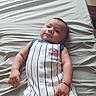 Julian is registered to the contest to win money with this photo: baby, infant, child, bed, sheet, clothing, onesie, striped, smile, cute, portrait, lying_down, bracelet, hand, face, skin, hair, indoor, young, person