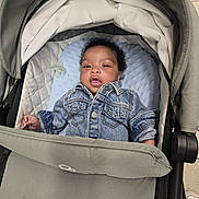 Omari-Momodou joined the competition — help win amazing prizes! baby, denim_jacket, stroller, pacifier, blue_cushion, infant, child, face, curly_hair, clothing, seated, indoor, person, cute, portrait, young_child, comfort, baby_gear, casual_wear, expression