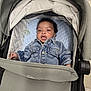 baby, denim_jacket, stroller, pacifier, blue_cushion, infant, child, face, curly_hair, clothing, seated, indoor, person, cute, portrait, young_child, comfort, baby_gear, casual_wear, expression