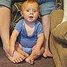 baby, child, infant, sitting, smiling, open_mouth, blue_outfit, family, adults, living_room, couch, carpet, indoor, portrait, face, eyes, arms, legs, barefoot, candid