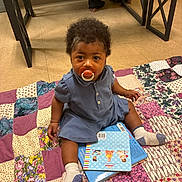 Heaven joined the competition — help win amazing prizes! toddler, pacifier, book, patchwork_quilt, socks, indoor, child, floor, curly_hair, blue_dress, barefoot_adult, wooden_bench, tile_floor, colorful, seated, curious, young_child, cozy, playtime, home
