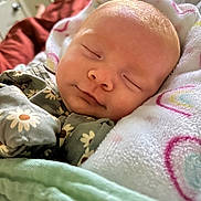 Ryleigh is registered to the contest to win money with this photo: baby, sleeping, blanket, floral_outfit, cozy, infant, face, peaceful, child, soft, cute, indoors, comfortable, wrapped, newborn, resting, portrait, head, skin, peace