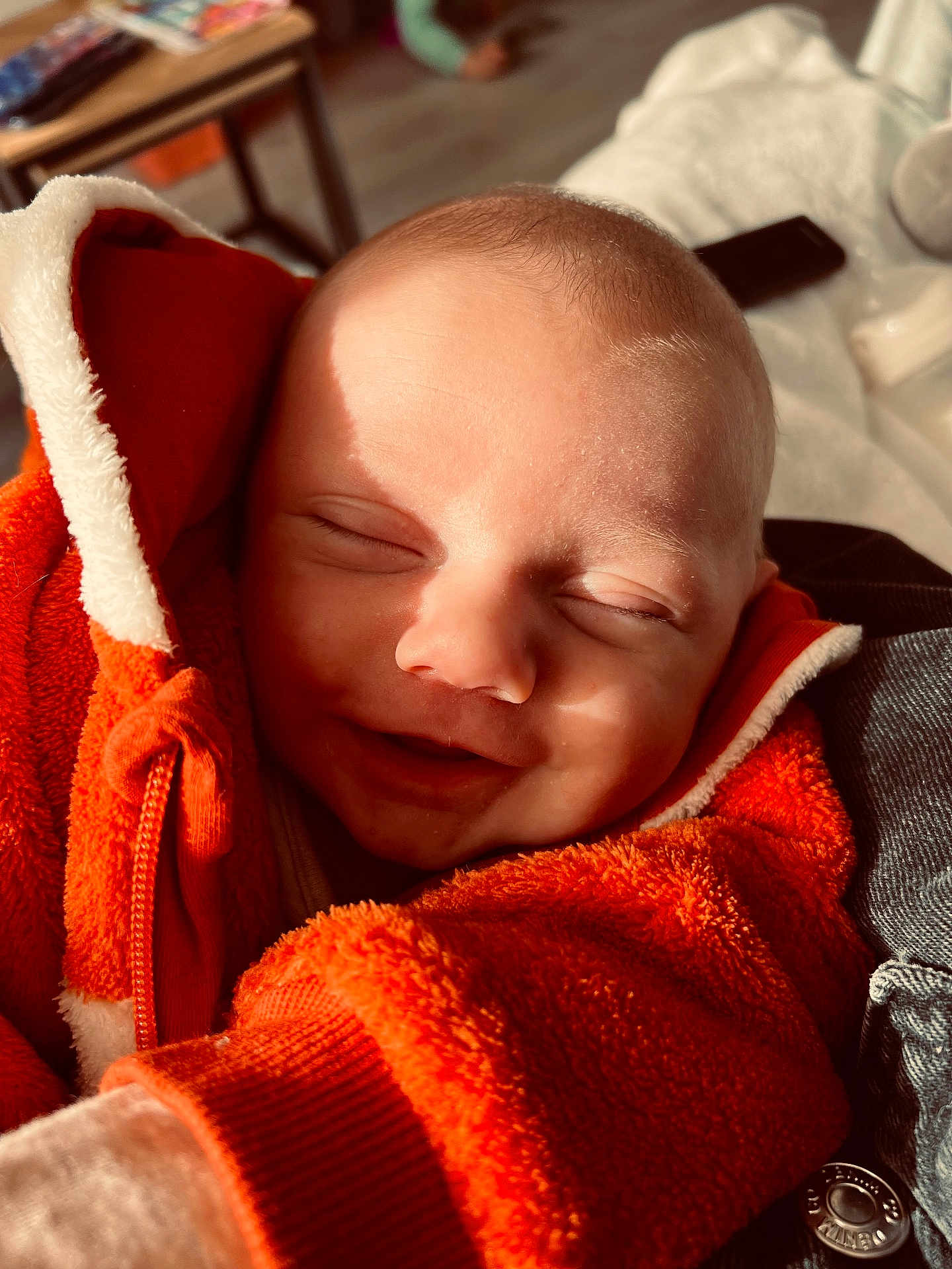 Owen a rejoint le concours — aidez-le/la à gagner de superbes lots ! baby, smiling, orange_jacket, fleece, cozy, close_up, face, infant, child, sunlight, shadow, warm, happy, portrait, indoor, cute, soft_texture, clothing, newborn, peaceful