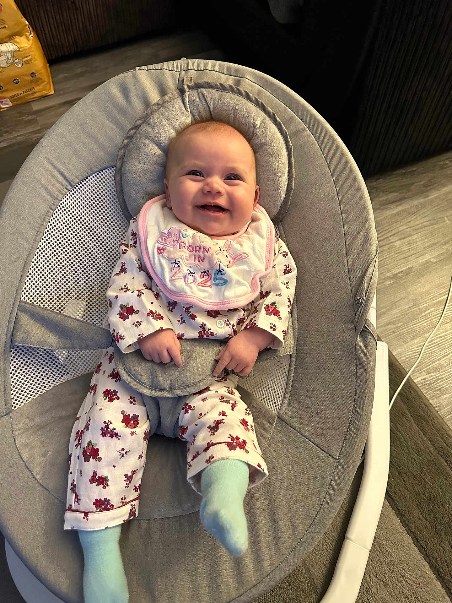 Daisy-Mae is registered to the contest to win money with this photo: baby, smiling, infant, bib, pajamas, baby_rocker, happy, indoor, floor, sock, child, cute, person, head, clothing, seat, home, face, comfort, joy