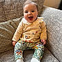 baby, child, smiling, sitting, couch, sweater, duck_design, floral_leggings, white_socks, happy, indoor, portrait, cute, face, person, furniture, cozy, home, patterned_clothing, infant