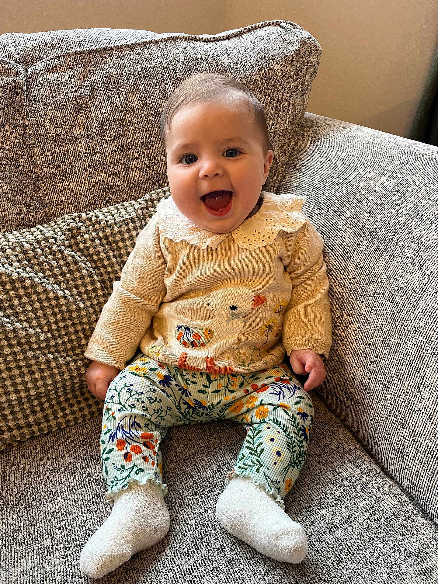 Georgia joined the competition — help win amazing prizes! baby, child, smiling, sitting, couch, sweater, duck_design, floral_leggings, white_socks, happy, indoor, portrait, cute, face, person, furniture, cozy, home, patterned_clothing, infant