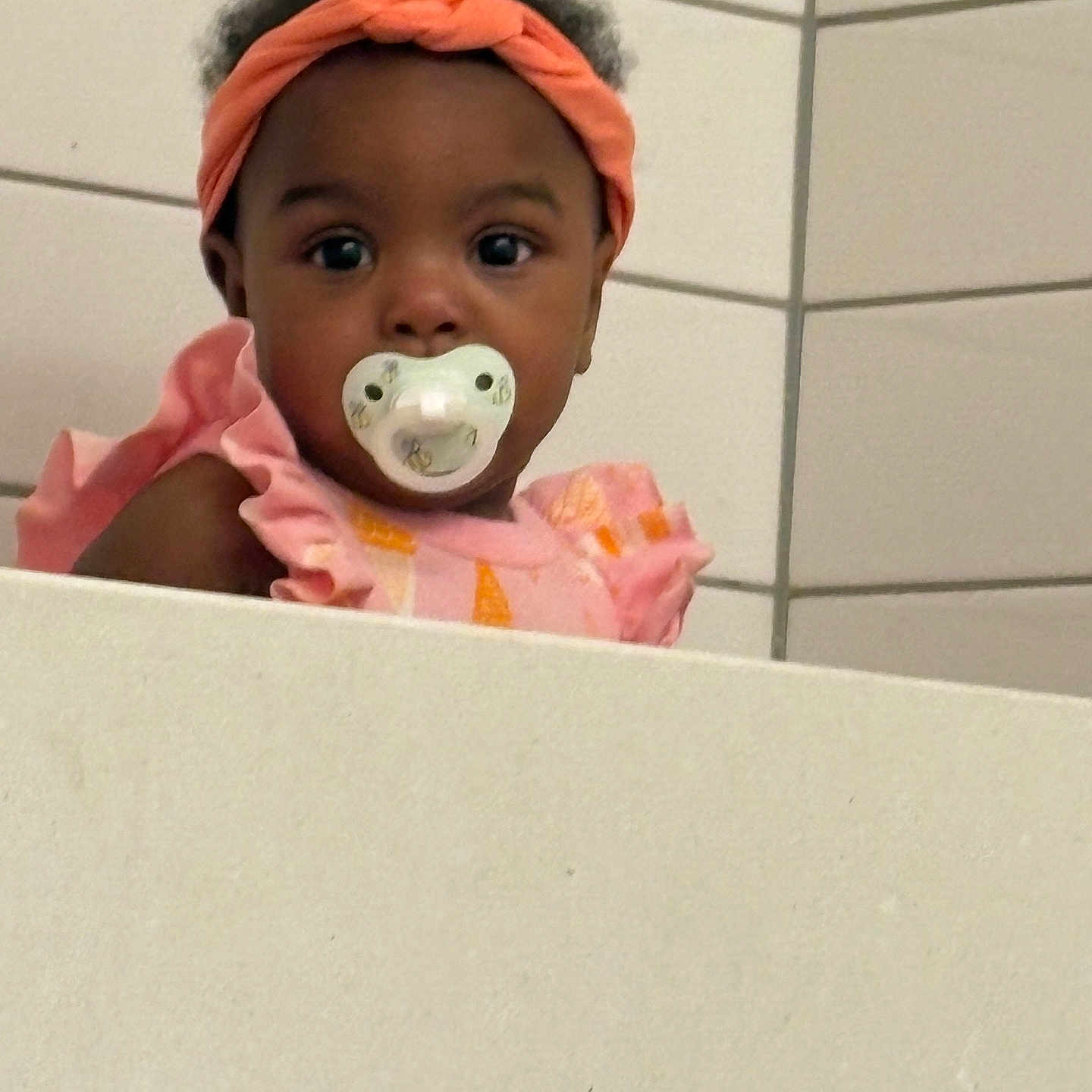 Amani joined the competition — help win amazing prizes! baby, child, closeup, curly_hair, cute, expression, face, fashion, headband, indoor, infant, ledgeline, looking, pacifier, person, pink_clothing, portrait, tile_wall, toddler, young_child
